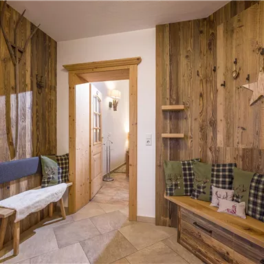 Ein gemütlicher Eingangsbereich mit Holzverkleidung und einer Sitzbank. An der Wand hängen Dekorationselemente wie Sterne und naturbelassene Äste.