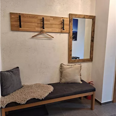 Ein moderner Eingangsbereich mit einer Holzbank und einem großen Spiegel. An der Wand hängt ein Garderobenständer mit Haken.