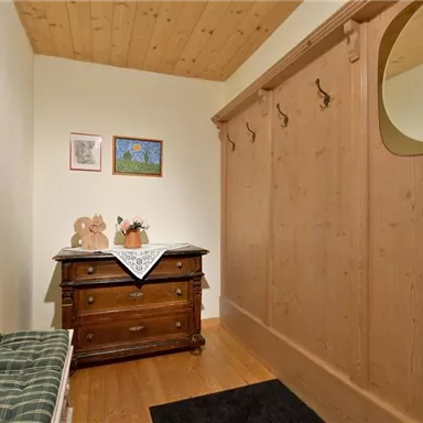A cozy entrance area with a wooden cabinet and a bench. Pictures hang on the wall, and there is a large mirror.