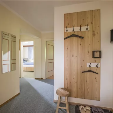 A bright hallway with a wooden panel and coat hooks. A stool and a mirror can be seen.