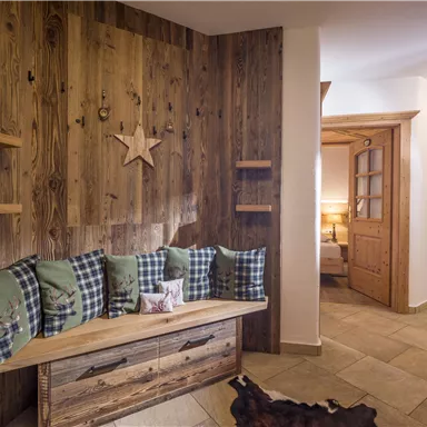 Ein gemütlicher Flur mit einer Holzwand und einer Bank, die mit karierten Kissen dekoriert ist. Der Raum hat eine warme und einladende Atmosphäre.