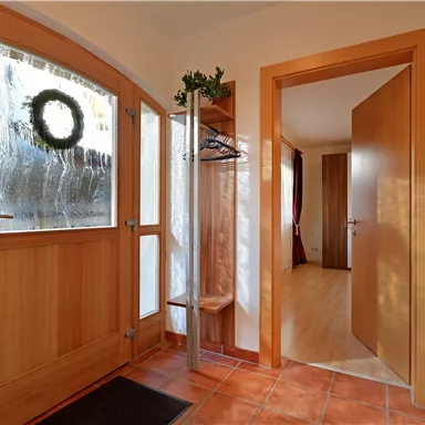 A bright entrance area with wood details and a decorative door wreath. In the background, doors to other rooms are visible.