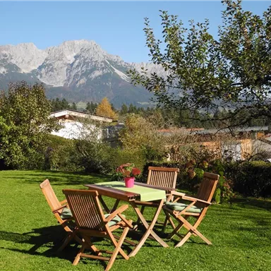 Ein schöner Garten mit einer Holztischgruppe und einer Blume in einem Topf. Im Hintergrund sind Berge und ein klarer Himmel zu sehen.
