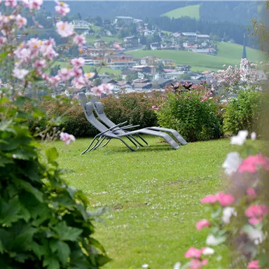 A garden with colorful flowers and lawn areas. In the background, there are sun loungers and a picturesque view of the landscape.