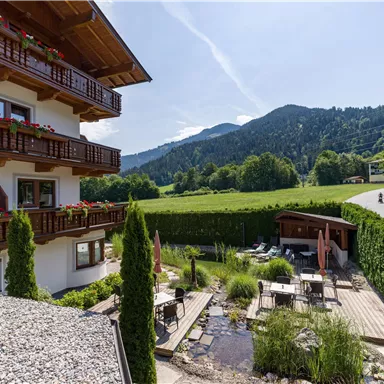 Ein gemütliches Hotel mit Balkon und Blumenbepflanzung. Der Blick reicht über grüne Wiesen und sanfte Hügel im Hintergrund.