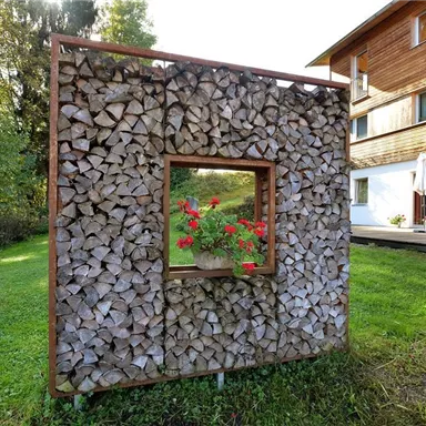 A creative wooden structure with a window displaying blooming flowers. In the background, a modern house and a green meadow can be seen.