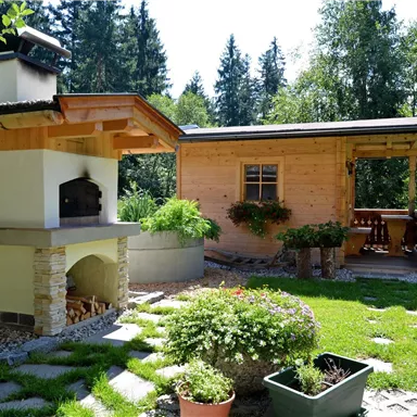 Ein gemütlicher Garten mit einem Grill und einer Holzunterkunft. Umgeben von Bäumen und einer gepflegten Rasenfläche.