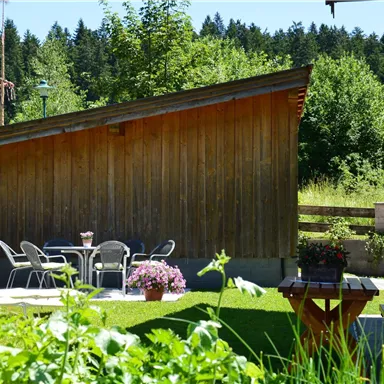 Ein schöner Garten mit einem Holzschuppen und einer Terrasse. Auf der Terrasse stehen Gartenmöbel und Blumen in Töpfen.