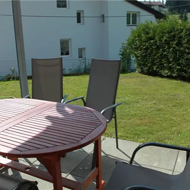 Ein gemütlicher Außenbereich mit einem runden Tisch und Stühlen. Im Hintergrund ist ein gepflegter Rasen und ein Teil eines Hauses sichtbar.