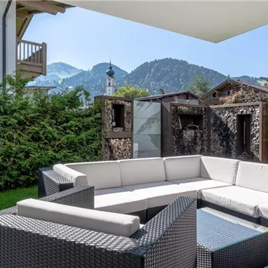 Ein schöner Außenbereich mit einer modernen Sofagarnitur und Blick auf die Berge. Die Grünpflanzen und die schattenspendende Überdachung schaffen eine einladende Atmosphäre.