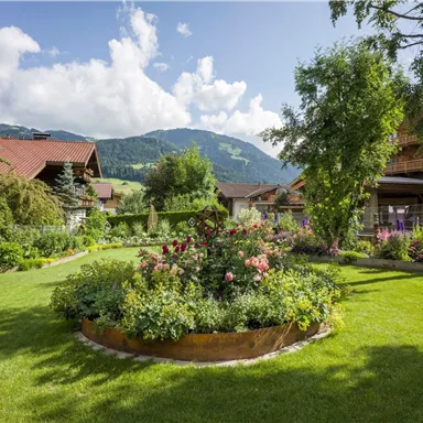 Ein schöner Garten mit bunten Blumen und gepflegtem Rasen. Im Hintergrund sind Berge und blauer Himmel zu sehen.