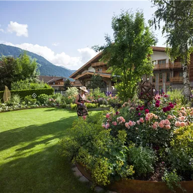 Ein schöner Garten mit bunten Blumen und grünem Rasen. Im Hintergrund sind Berge und Holzgebäude zu sehen.