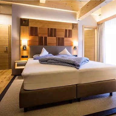 Ein modernes Schlafzimmer mit einem großen, bequemen Bett und hellen Holztönen. Große Fenster lassen viel Tageslicht herein und schaffen eine einladende Atmosphäre.