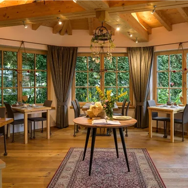 Ein einladendes Restaurant mit Holzdecken und großen Fenstern. Tische sind liebevoll gedeckt und frische Blumen stehen im Mittelpunkt.