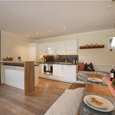 Eine moderne und helle Küche mit weißen Möbeln und Holzdetails. Gemütliche Sitzecke mit Tisch und dekorativen Elementen.