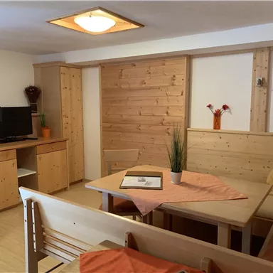 Ein gemütlicher Wohnraum mit Holzmöbeln und einem Tisch. Auf der Ablage stehen Blumenvasen und ein Fernseher ist zu sehen.