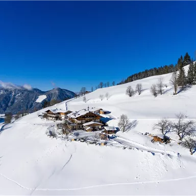 Eine malerische Winterlandschaft mit schneebedeckten Hügeln und Holzhäusern. Der klare blaue Himmel vervollständigt das idyllische Bild.