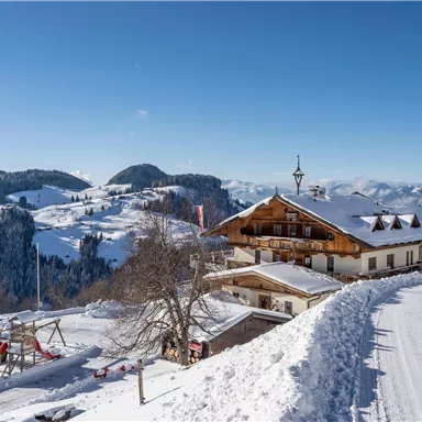 Ein malerisches Bergdorf im Schnee mit einem traditionellen Holzhaus. Der klare Himmel und die schneebedeckten Hügel schaffen eine idyllische Winterlandschaft.