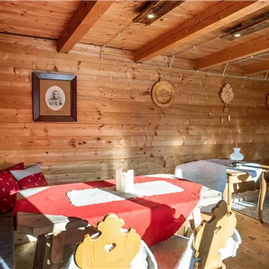 Ein gemütlicher Raum mit Holzverkleidung und rustikalen Möbeln. Der Tisch ist mit einer roten Tischdecke gedeckt, und die Wände zieren einige dekorative Teller.