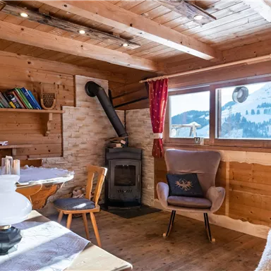 Ein gemütlicher Raum mit Holzwänden und einem Kamin. Der Arbeitsplatz ist hell und einladend, mit Blick auf die Berge durch ein großes Fenster.