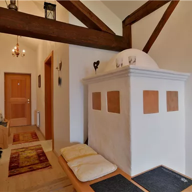 An inviting hallway with wooden beams and a cozy stove. The walls are light, and the space feels friendly and warm.