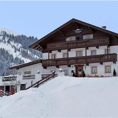 A cozy chalet in a snowy mountain landscape. The surroundings are surrounded by snow-covered mountains and the sky is clear.