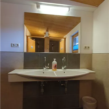 Ein modernes Badezimmer mit einem großen Waschbecken und einem Spiegel. Die Wände sind elegant in neutralen Farbtönen gestaltet und es gibt Holzdeckenelemente.