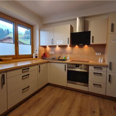 Eine moderne Küche mit Holzdetails und einem großen Fenster. Die Ausstattung umfasst einen Herd, einen Kühlschrank und verschiedene Küchengeräte.