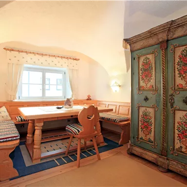 Ein gemütlicher Essbereich mit einer Holztischgruppe und einer bunten, bemalten Kommode. Die Wände sind hell, und das Licht fällt freundlich durch das Fenster.