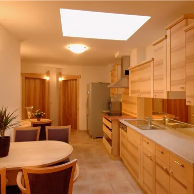 A modern kitchen with light wood cabinets and a dining area. A skylight provides plenty of daylight in the room.