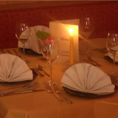 Ein elegant gedeckter Tisch mit gefalteten Servietten und Gläsern. Eine Kerze und eine Menükarten sind ebenfalls vorhanden.