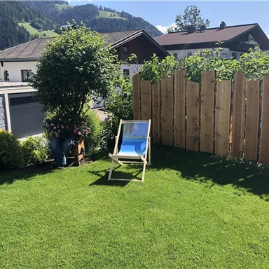 A beautiful garden with green grass and a lounge chair. In the background, wooden cladding and some trees can be seen.