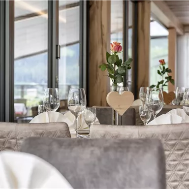 Ein elegantes Restaurant mit modernen Möbeln und großen Fenstern. Tische sind schön gedeckt mit Gläsern und Blumen in vasen.