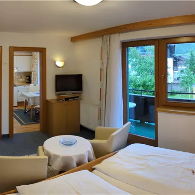 Ein gemütliches Hotelzimmer mit zwei Betten, einem Tisch und Sessel. Große Fenster bieten Blick auf die Natur draußen.