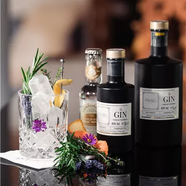 Ein stilvolles Arrangement aus Gin-Flaschen und einem Cocktailglas mit Eis und frischen Kräutern. Die Szene ist elegant und ansprechend, ideal für einen gemütlichen Abend.