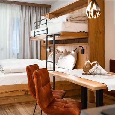 A cozy room with a double bed and a loft bed. The room is modernly furnished and features a dining area with a table and chairs.