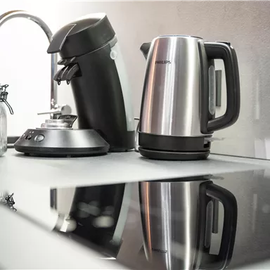 A modern kitchen corner with a kettle and a coffee maker. The shiny cooktop reflection showcases the appliances elegantly.