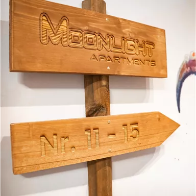 A wooden sign with the inscription "Moonlight Apartments" and the direction to numbers 11-15. The sign is simply designed and gives a rustic impression.