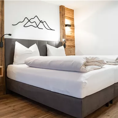 A modern bedroom with a double bed and wooden decor. Stylized mountain motifs and lights are mounted on the wall.