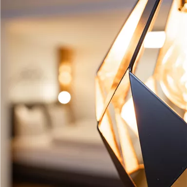 A modern lamp in geometric shape hangs in the foreground. In the background, a bright, stylish room can be seen.