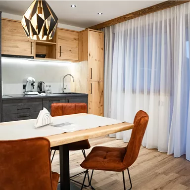 A modern kitchen with a wooden dining table and stylish chairs. Large windows let in plenty of light.