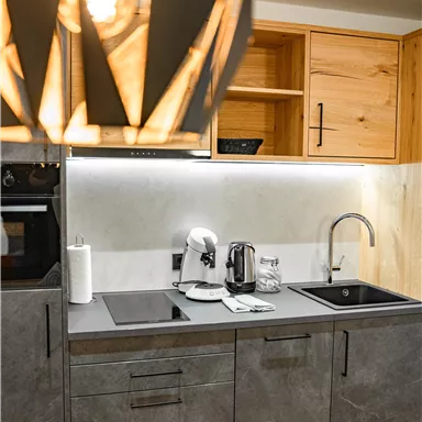 A modern kitchen with gray cabinets and wooden shelves. The equipment includes a coffee machine, a kettle, and a sink.