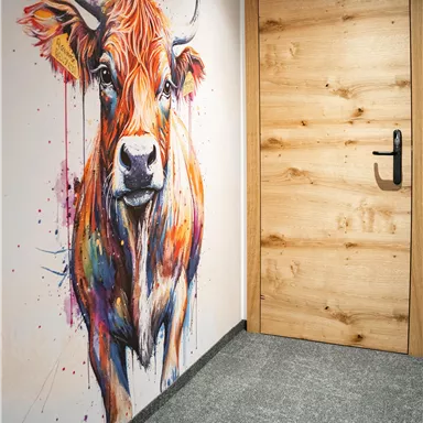 A colorful mural of a cow in a modern setting. Next to it, a wooden door that closes off the space.