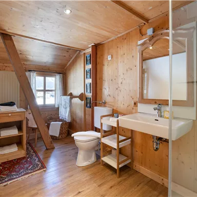 Ein gemütliches Badezimmer mit Holzwänden und einem großen Fenster. Es verfügt über eine Dusche, ein Waschbecken und eine Toilette.