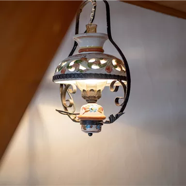 Eine dekorative Tischlampe hängt von der Decke. Sie hat ein kunstvolles Design mit farbigen Verzierungen und strahlt warmes Licht aus.