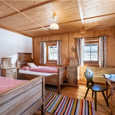 Ein gemütliches Holzschlafzimmer mit zwei Betten, einem Tisch und Stühlen. Die Wände sind mit Holzpanelen verkleidet, und große Fenster lassen viel Licht herein.