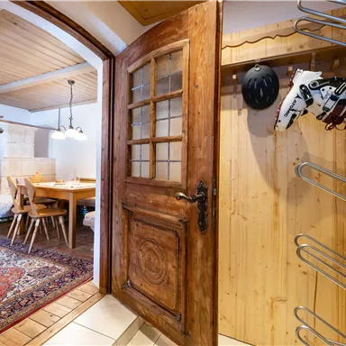 Ein einladender Eingangsbereich mit einer schönen Holztür und einem Garderobenständer. Im Hintergrund ist ein Essbereich mit einem Tisch und Stühlen zu sehen.