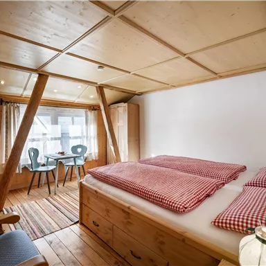 Ein gemütliches Schlafzimmer mit Holzverkleidung und zwei Einzelbetten. Im Hintergrund befinden sich ein Tisch und Stühle sowie ein Fenster mit Vorhängen.