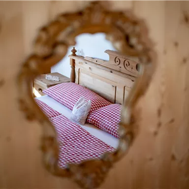 Ein gemütliches Schlafzimmer mit einem Holzbett und karierten Kissen. Der Blick ist durch einen eleganten Spiegel gerahmt.
