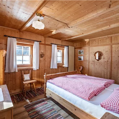 Ein gemütliches Schlafzimmer mit Holzverkleidung und einem großen Bett. Die Fenster lassen viel Licht hinein, und die Einrichtung ist einfach und einladend.
